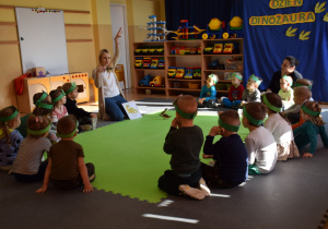 Dzieci siedzą w kole, nauczycielka prezentuje dinozaury